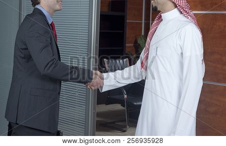 Middle Eastern And Caucasian Businessmen Shaking Hands, In An Office