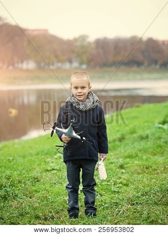 Child With Quadrupter In Autumn Scarf And Coat Standing At River Water On Green Grass On Natural Bac