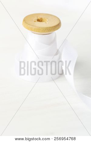Single Wooden Spool Roll With Curly Silk Ribbon On White Wood Background. Sewing Crafts Hobby Concep