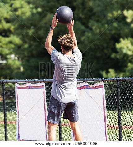 A High School Track Runner Is Throwing A Medicine Ball Over His Head During Strength And Coordinatio