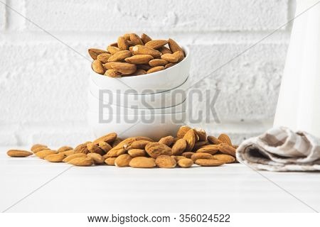 Dried almonds nuts in bowl on white table before white brick wall.
