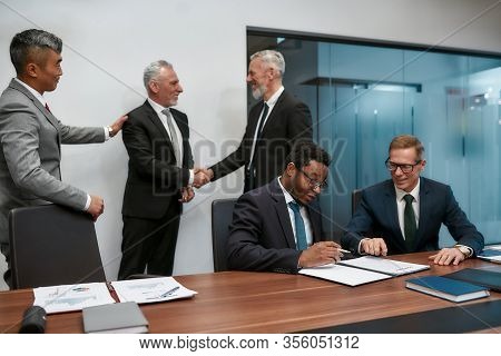 Confident African Businessman Reading A Contract And Discussing Something With His Partner While Two