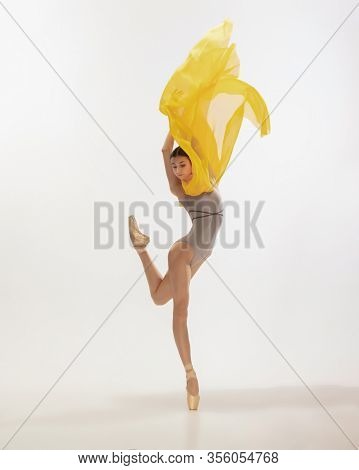 Graceful Classic Ballerina Dancing, Posing Isolated On White Studio Background. Bright Yellow Cloth.