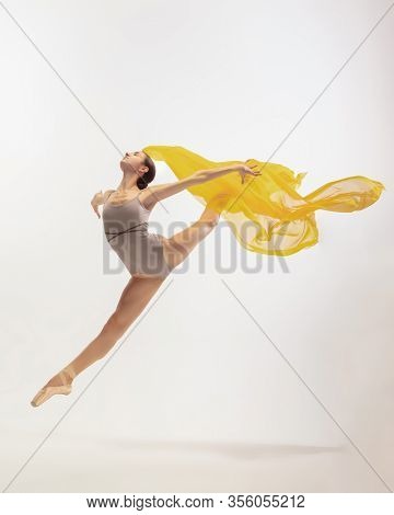 Graceful Classic Ballerina Dancing, Posing Isolated On White Studio Background. Bright Yellow Cloth.