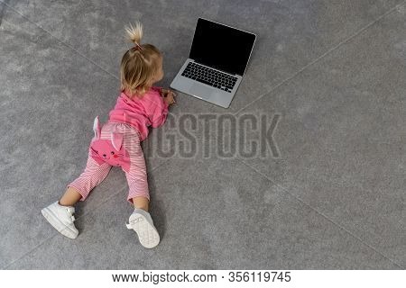 Small Cute Blond Caucasian Interested Baby Laying On Grey Rug On Floor And Watching Tv On Laptop, Bl