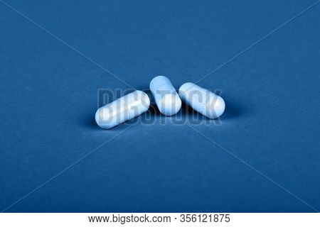 Close Up Three White Gel Cap Pills Of Medicine Over Dark Blue Background With Copy Space, High Angle
