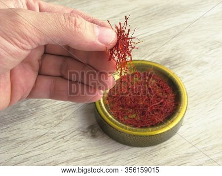 Iranian Dried Red Saffron In Male Hand On Wooden Background. Saffron Threads. Luxury Spice.