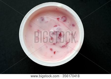 Cream Yogurt In A Plastic Cup On A Black Background. Curds Products With Raspberries Top View. Yogur