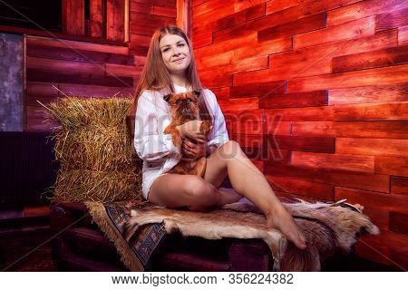 Beautiful Girl In White Shirt With Small Dog On The Couch With Hay In The Barn Or In The Hayloft Wit