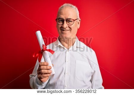 Middle age hoary student man wearing glasses holding university graduated degree diploma with a happy face standing and smiling with a confident smile showing teeth