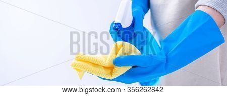 Young Woman Housekeeper In Apron Is Cleaning, Wiping Down Table Surface With Blue Gloves, Wet Yellow