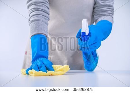 Young Woman Housekeeper In Apron Is Cleaning, Wiping Down Table Surface With Blue Gloves, Wet Yellow