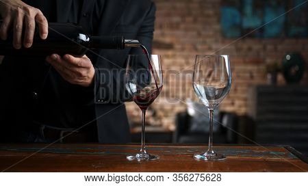 Elegant man pouring red wine from wine bottle to wine glasses at home in a cosy dark room.