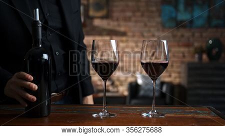 Elegant man tasting and serving red wine in a couple of wine glasses at home in a cosy dark room.
