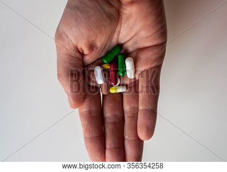 Male Hand Keeping Pills Of Diffetent Colors On White Background