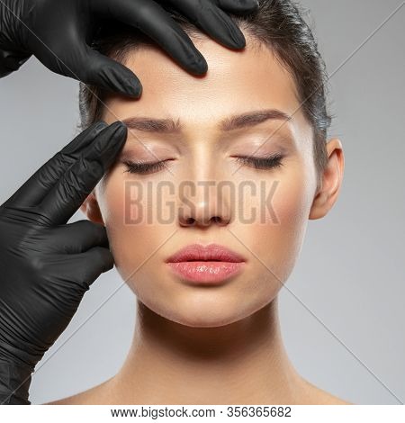 Face skin check before plastic surgery. Beautician touching woman face. Doctor checks a skin before plastic surgery. Beauty treatments. Plastic surgery doctor is touching face of a patient by hands
