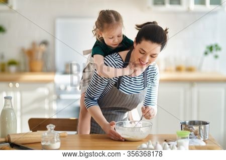 Happy loving family are preparing bakery together. Mother and child daughter girl are cooking cookies and having fun in the kitchen. Homemade food and little helper.                                