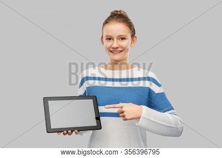 technology and people concept - happy smiling teenage girl in pullover showing tablet pc computer over grey background