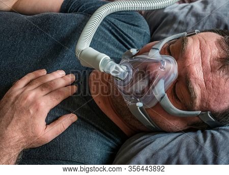 A man in an oxygen mask for CPAP therapy in bed