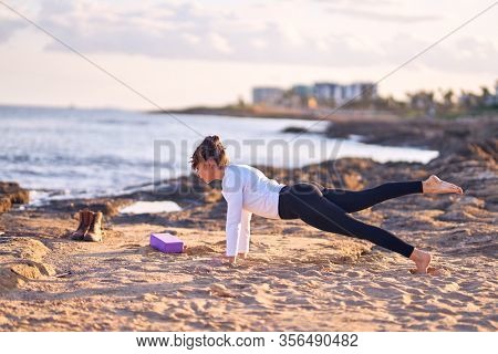 Young beautiful sportwoman practicing yoga. Coach teaching plank pose at the beach