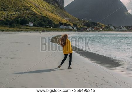 Back Of Girl In Yellow Jacket On The White Sand  Beach In Ramberg On Lofoten Islands, Norway