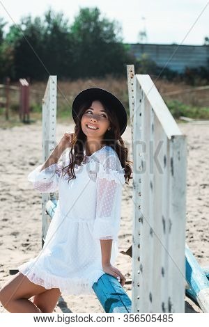 Beautiful Sexy Girl Posing On The Horizontal Crosspiece On A Horse Epodrom. Female Wearing White Dre