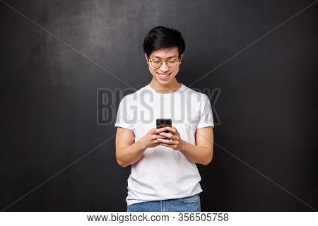 Technology, Gadgets And People Concept. Smiling Teenage Asian Guy Playing On Phone, Texting Friend U
