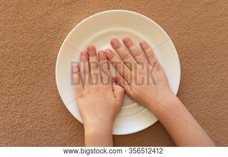 Childrens Little Hands Lie In An Empty White Plate On The Table