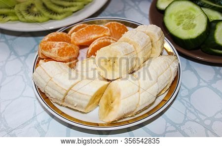 On A Light Saucer, A Banana Is Cut Into Circles And Tangerine Slices Are Sprea