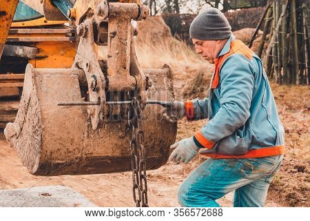 The Worker Grabs Chains Onto The Excavator Bucket To Carry And Install Concrete Slabs On The Road.