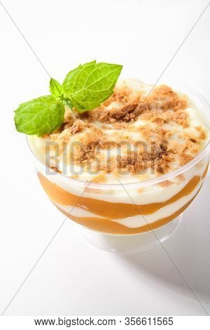 Dessert with mango, vanilla cream and cookie crumbs in restaurant glass isolated. Delicious fruit blancmange with apricots, prepared panna cotta or creamy mousse on white table closeup
