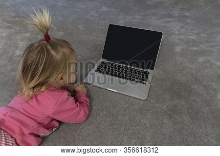 Small Cute Blond Caucasian Baby Laying On Floor On Grey Rug And Watching Cartoons On Laptop With Gre