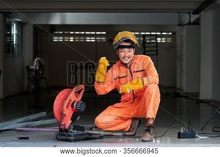 The Steelworker Poses Confidently At His Work Site. Metal Grinding On Steel Spare Part In Workshop. 