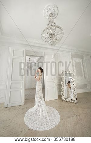 Beautiful Bride Posing In Wedding Dress In A White Photo Studio. Mirror. Sofa. Bouquet. The Door. Ch