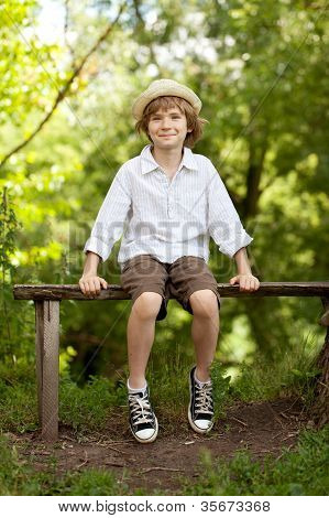 Boy In The Hat And Shorts Sitting On A Bench