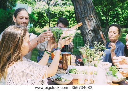 Cheerful Young People At Table In Yard. Happy Young Male And Female Friends Gathering Around Table W
