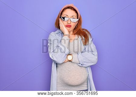 Young redhead pregnant woman expecting baby wearing funny thug life sunglasses thinking looking tired and bored with depression problems with crossed arms.