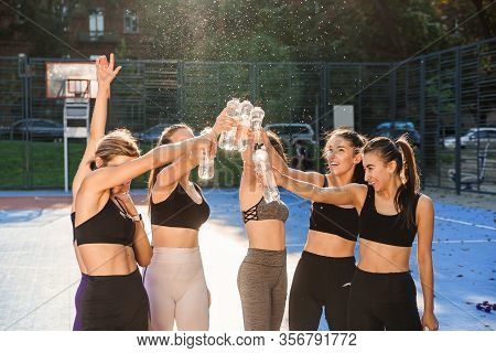 Four Good-looking Cheerful Slender Ladies In Sportswear Relaxing On The Sportground And Holding In T