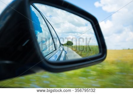 Side Rear-view Mirror Car Reflection Of A Winding Road In A Forest Or Countryside. Dramatic Scenery