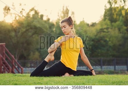 Young Attractive Woman Practicing Yoga In The Park At Sunset. Outdoor Sport Activity. Practice Yoga 