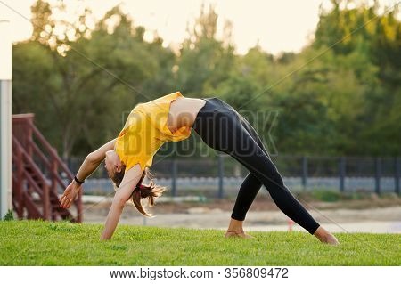 Young Attractive Woman Practicing Yoga In The Park At Sunset. Outdoor Sport Activity. Practice Yoga 