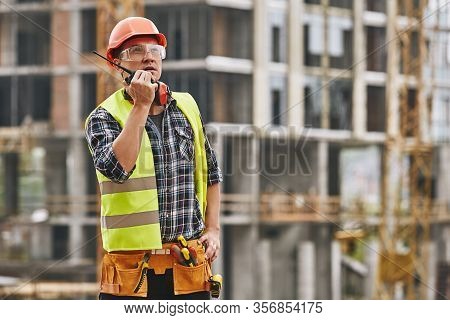 Hecking Work. Professional Young Builder In Working Uniform And Red Protective Helmet Talking To Cra