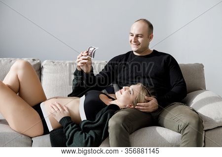 Couple Of Handsome Husband And Pretty Pragnant Woman Posing At Studio Embracing Stomach. Young Styli