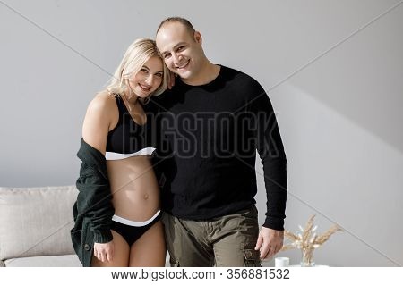 Couple Of Handsome Husband And Pretty Pragnant Woman Posing At Studio Embracing Stomach. Young Styli