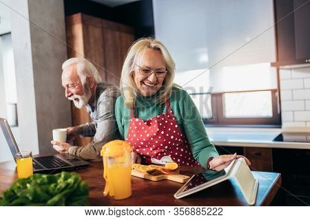 Happy Retired Couple Browsing The Internet Together On A Laptop Computer And Digital Tablet.quaranti