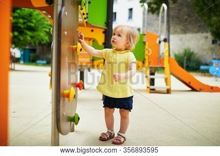 Adorable Toddler Girl On Playground Near Slide. Child Playing On The Street. Outdoor Activities For 