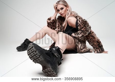 Young blonde woman in leopard coat and boots sitting in studio