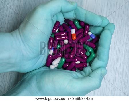 Inverted Colors Male Hands Keeping A Lot Of Pills Of Diffetent Colors On Wooden Table Background. Ma