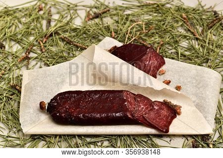 Dried Sausage Made Of Roe Meat On Parchment With Pine Buds At The Bottom. Flooring Made Of Pine Need