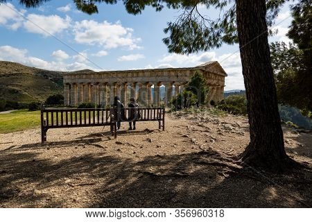 Segesta, Sicily - February 9, 2020: People Relaxing On A Bench In Front Of The Ancient Doric Temple 